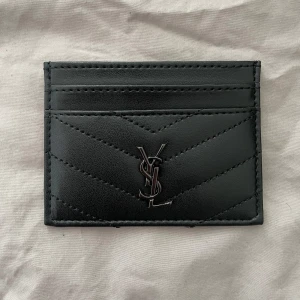 YSL kortficka - Snygg svart plånbok från YSL i äkta skinn och metallogo framtill, helt ny oanvänd kommer i plast. Plånboken har flera kortfack, perfekt för dig som vill ha något både stilrent och lyxigt i fickan, pris kan diskuteras vid snabb affär.