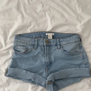 Ljusblå jeansshorts från H&M - Snygga ljusblå jeansshorts från H&M i klassisk femficksmodell. Shortsen har upprullade benslut, bälteshällor och dragkedja med knapp. Perfekta för varma dagar och enkla att matcha med allt. Stl 36.