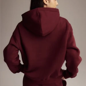 Vinröd oversized hoodie med huva - Mysig vinröd hoodie med stor huva och magficka. Oversized passform och långa ärmar gör den perfekt för chill dagar. Tillverkad i mjuk bomullsblandning som känns skön mot huden. Enkel och stilren design utan tryck eller mönster.