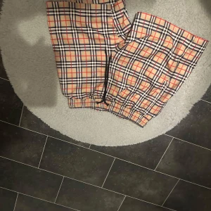 Rutig Burberry shorts med snörning - Snygga shorts från Burberry i klassiskt rutigt mönster med beige, svart, röd och vit. De har elastisk midja med snörning och är tillverkade i ett lätt och bekvämt material, perfekt för sommaren. Passar dig som vill sticka ut med en ikonisk stil.