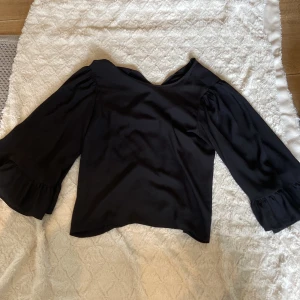 Svart blus med volangärm från Zara - Supersnygg svart blus från Zara med vida, långa ärmar och volangdetalj vid ärmslut. Blusen har en lätt glansig finish och en klassisk, något lös passform. Perfekt för dig som gillar stilrena och trendiga plagg💗