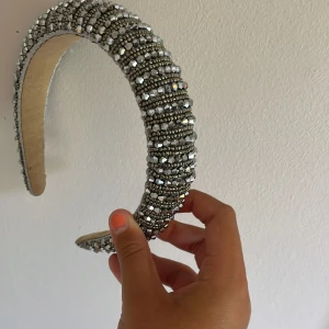Glittrigt diadem med silverpärlor - Säljer ett chunky diadem täckt av glittrande silverfärgade pärlor och stenar. Diademet är brett och ger en riktigt statement-look, perfekt om du vill sticka ut. Insidan är klädd i beige tyg för extra komfort. Superfint till både utsläppt och uppsatt hår.