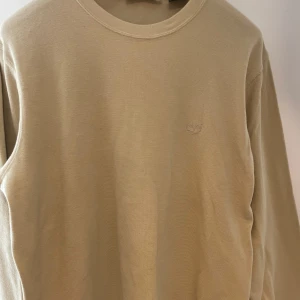 Beige långärmad tröja Timberland XL - Snygg beige långärmad tröja från Timberland i 100% bomull. Tröjan har en enkel och clean look med rund halsringning och diskret broderad logga på bröstet. Perfekt för dig som gillar stilrena basplagg med lite oversized känsla.