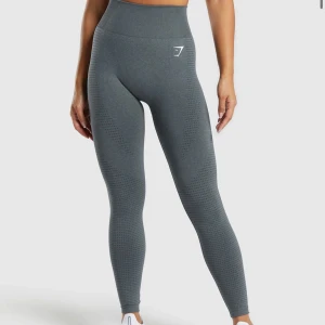 Grå seamless leggings från Gymshark - Säljer ett par grå seamless leggings från Gymshark i kollektionen ”Vital Seamless Leggings” med hög midja och diskret mönster längs benen. De är tighta och stretchiga, perfekta för träning. Materialet är mjukt och följsamt med logga framtill och vid vristen💖stl S men passar även de som vanligtvis bär XS