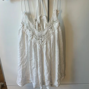 Vit linnetopp med spets från KappAhl - Supersöt vit linnetopp från KappAhl Vintage Stories med tunna axelband och vacker spetsdetalj upptill. Toppen har en luftig, lite skrynklig struktur och är perfekt för varma dagar. Snygg att styla med jeans eller kjol för en chill sommarlook.