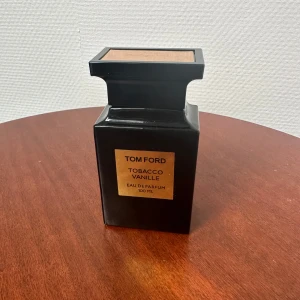Tom Ford Tobacco Vanille 100ml EdP - Tom Ford Tobacco Vanille Eau de Parfum i en lyxig svart, fyrkantig glasflaska med guldbrun etikett och lock. Flaskan rymmer 100 ml och har en elegant, modern design som verkligen sticker ut på hyllan. Perfekt för dig som gillar exklusiva dofter med karaktär.