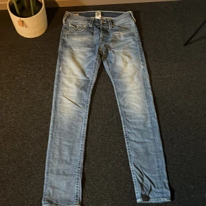 True Religion ljusblå slim - Säljer ett par ljusblå skinny jeans från True Religion med ikoniska bakfickor och snygga kontrastsömmar. Jeansen har normal passform, låg midja och är tillverkade i bomull med lite stretch. Perfekta för dig som gillar streetstyle och vill sticka ut.