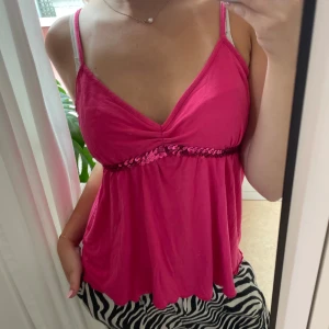 Rosa y2k topp med paljetter - Y2k topp som funkar perfekt till fest eller till vardags. Märket saknas då den är köpt på vinted.  Linnetopp med smala axelband och v-ringning. Toppen har en glittrig rad av rosa paljetter under bysten som ger extra bling. Luftig och flowy passform, perfekt för varma dagar eller när du vill sticka ut lite extra.💕 Den är i S/M