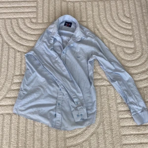 Ljusblå skjorta från Paris Star M - Snygg ljusblå skjorta från Paris Star i 100% bomull. Klassisk modell med krage, knappar framtill och broderad logga på bröstet. Perfekt för dig som gillar stilrena och enkla plagg med en fräsch vibe.