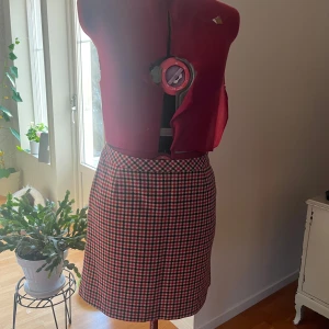 Rutig kortkjol från GANT i ullmix - Supersnygg rutig kortkjol från GANT i rött, svart och vitt. Kjolen har klassiskt mönster, dragkedja i sidan och är gjord i en ullmix som känns både trendig och tidlös. Perfekt för dig som vill sticka ut med en preppy vibe.