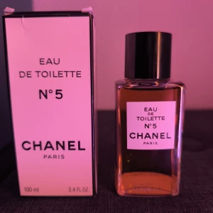 Vintage Chanel No 5 Eau de Toilette 100ml Splash - Vintage Chanel No 5 Eau de Toilette i klassisk fyrkantig splash glasflaska med svart lock. Parfymen är bärnstensfärgad och kommer i originalkartong. Volymen är 100 ml och flaskan har en stilren, tidlös design med tydlig Chanel-logga. Tillverkad i Frankrike.