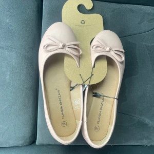 Ljusa ballerinaskor med rosett - Söta ljusrosa ballerinaskor från Claudia Ghizzani med rund tå och dekorativ rosett framtill. Skorna har en klassisk, feminin design och är tillverkade i syntetmaterial med mjuk innersula för extra komfort. Helt nya