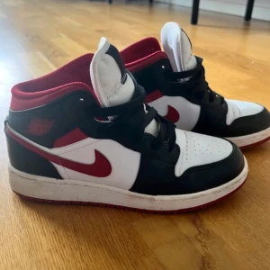Nike Air Jordan 1 Mid svart/röd/vit - Röda jordan air skor, höga modellen. Använda ett fåtal gånger och är i väldigt fint skick!   Nypris: 2600kr   Storlek: 37,5