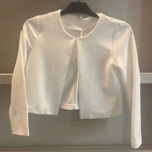 Vit öppen cardigan jacka från C - Snygg vit cardigan jacka från C i storlek 146. Jackan är öppen framtill utan knäppning, har lång ärm och är tillverkad i ett lätt strukturerat tyg. Perfekt för dig som gillar en clean och stilren look.