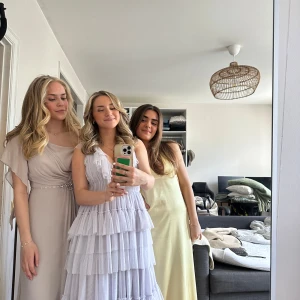 Ljuslila volangklänning med v-ringning - Superfin långklänning i lila med flera lager volanger och v-ringning. Klänningen har ärmlös design , perfekt för bal. 