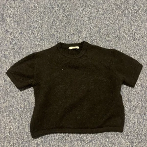 Svart stickad croppad tröja Gina Tricot - Svart stickad tröja från Gina Tricot med kort ärm och croppad passform. Enkel och stilren med rund halsringning, perfekt till jeans eller kjol. Mjuk och skön känsla, passar dig som gillar minimalistisk stil.