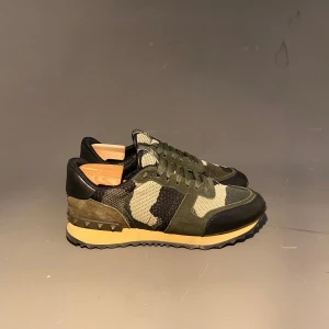 Valentino Garavani Rockrunner sneakers - Snygga Valentino Rockrunner sneakers i camouflage med gröna, svarta och beige toner. Skorna har snörning, detaljer i mocka och skinn samt en cool nubbad häl. Perfekta för dig som vill sticka ut med stilrena och lyxiga sneakers.