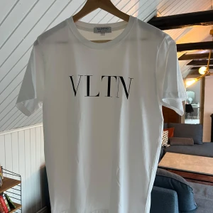 Vit VLTN t-shirt från Valentino - Vit t-shirt från Valentino med svart VLTN-tryck på bröstet. Väldigt true to size och sitter bra på mig som brukar ha L. Passar även M om man gillar lite mer oversize. Perfekt nu inför sommaren.