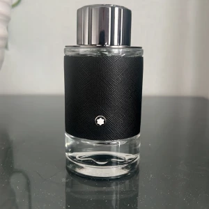Montblanc Explorer Eau de Parfum - Montblanc Explorer Eau de Parfum i en stilren rund glasflaska med svart texturerad läderdetalj och silverfärgat lock. Flaskan har Montblancs ikoniska stjärnlogo framtill och på locket. Perfekt för dig som gillar exklusiva och maskulina dofter.