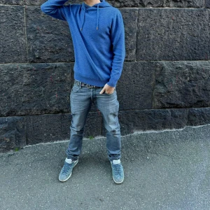 Blå Merino-Ull hoodie, justerbar huva - Säljer en blå Merino-Ull hoodie med huva och snörning. Tröjan har en avslappnad passform och är tillverkad i mjukt material som passar perfekt för kyliga dagar. Enkel och stilren design utan tryck eller mönster, perfekt att slänga på sig när du vill vara både bekväm och snygg.