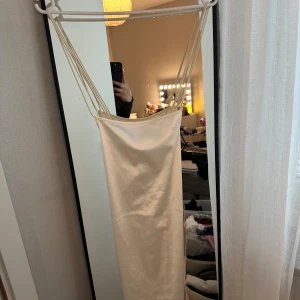 Champagnefärgad satinklänning - Säljer en elegant champagnefärgad långklänning i satin med tunna axelband. Klänningen har en slimmad passform och en stilren, minimalistisk look som passar perfekt till speciella tillfällen.