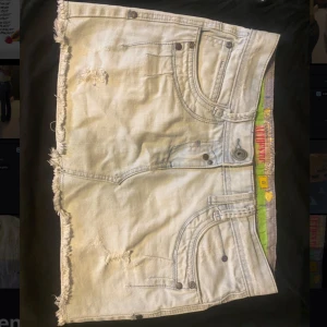 Ljus mini jeanskjol Lågmidjad - Snygg ljusblå jeanskjol från Authentic Denim med  slitna detaljer. Den är lowwaist i modellen och kort/ i mini format. Coola detaljer och sliten.