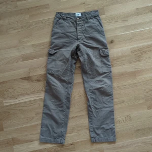 Grå cargobyxor från Rocky, medium - Säljer ett par grå cargobyxor från Rocky i storlek medium. Byxorna har raka ben, stora fickor på sidorna och knäppning med knappar. Tillverkade i bomull för en skön och avslappnad känsla. Perfekta för en chill och casual stil.