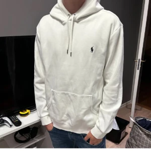 Vit Ralph Lauren hoodie - Snygg vit hoodie från Polo Ralph Lauren med klassisk broderad logga på bröstet. Tröjan har huva med snörning, känguruficka och långa ärmar. Perfekt för en clean och stilren look. Tillverkad i mjuk bomull för extra komfort.