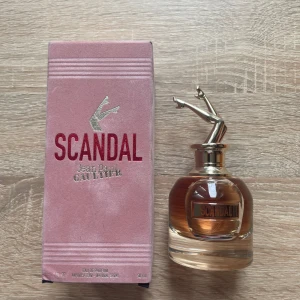 Scandal parfym Jean Paul Gaultier - Scandal Eau de Parfum från Jean Paul Gaultier i en unik glasflaska med guldiga ben som lock. Parfymen har en rosa-beige kartong med sammetsyta och tydlig logga. Doften är söt, fruktig och blommig. Flaskan rymmer 50 ml och har bara testats en gång.