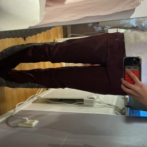 Vinröda byxor med leoparddetalj - Unika vinröda byxor med utsvänga ben och grå leopardmönstrade paneler längs sidorna. Byxorna har normal passform och är tillverkade i ett mjukt bomullstyg. Perfekta för dig som vill sticka ut med en cool detalj i vardagslooken.