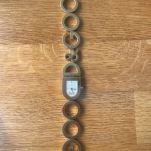 Guldig D&G armbandsklocka - Unik armbandsklocka från D&G i guldig färg med coola länkar som bildar D&G-loggan. Batteriet är just bytt och storleken går att justera på armbandet med extrabitarna.