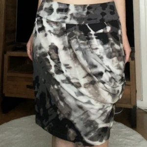 Mönstrad silkeskjol från Wera - Supersnygg kortkjol i siden från Wera med abstrakt svart, grå och vit mönstring. Kjolen har draperad detalj framtill som ger en cool och modern look. Perfekt för dig som vill sticka ut med en unik och trendig stil.