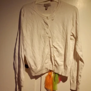 Vit kofta med knappar - Vit kofta med rund hals och långa ärmar. Stängs med flera små knappar framtill. Enkel och klassisk design som passar till mycket. Tillverkad i mjukt material, perfekt för lager-på-lager-stil.