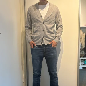 Grå kofta med knappar - Snygg grå kofta med v-ringning och knappar framtill. Tröjan har två fickor.  Perfekt för lager-på-lager och passar till både jeans och chinos. Enkel och stilren design som funkar året runt.