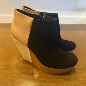 Beige och svarta kilklackade stövletter - Unika stövletter med kilklack i beige och svart. Ovandelen är i svart mocka och beige skinn, med dragkedja i guld baktill. 