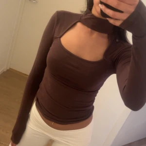Brun långärmad topp - Säljer en brun långärmad topp med tight passform och unik halsringning som går upp runt halsen. Toppen är figurnära och har en snygg, modern design som sticker ut. 