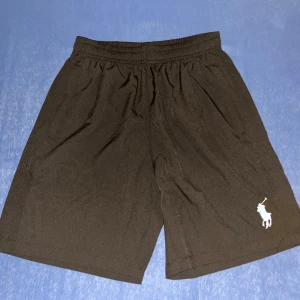 Svarta shorts från Polo Ralph Lauren - Svarta shorts från Polo Ralph Lauren med elastisk midja och klassisk vit logga på ena benet. De är enkla och stilrena, perfekta för chill dagar eller träning. Materialet känns lätt och svalt, vilket gör dem grymma för sommaren.