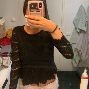 Svart spetsblus med volangkant - Supersnygg svart blus i spets med långärmade ärmar och volangkant nertill. Transparenta partier på ärmarna ger en extra cool touch. Perfekt att styla med jeans eller kjol för en trendig look.