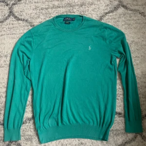Grön tröja från Polo Ralph Lauren - Slim fit grön tröja från Polo Ralph Lauren i mjuk pima bomull. Klassisk rund halsringning och diskret broderad logga på bröstet. Långärmad modell med ribbade muddar och nederkant. Perfekt för dig som gillar stilren och enkel design.