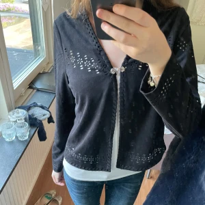 Svart bolero/kofta med broderade detaljer! - Svart bolero/kofta från Flash Woman med v-ringning och snygga broderade håldetaljer längs ärmar, nederkant och hals. Stängs framtill med en dekorativ silverspänne. Mjuk känsla och långärmad, aldrig andvänt💞