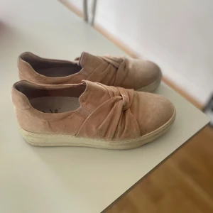 Beige mockasneakers från K.Cobler - Snygga sneakers i beige mocka från K.Cobler med rund tå och platt sula. Skorna har en cool knutdetalj framtill som ger en unik look. Perfekta för dig som gillar stilrena men ändå trendiga skor.