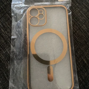 Genomskinligt mobilskal med gulddetaljer - Snyggt genomskinligt mobilskal med guldfärgad ram och MagSafe-ring. Skalets design har markerade kamerahål och passar perfekt för dig som vill ha en stilren look med lite extra bling.