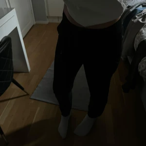 Svarta mjukisbyxor Peak Performance S - Svarta mjukisbyxor från Peak Performance med broderad logga på höften. Byxorna har en bekväm resår i midjan och är gjorda i mjukt material med fleece på insidan. Perfekta för chill eller träning, klassisk och stilren look.