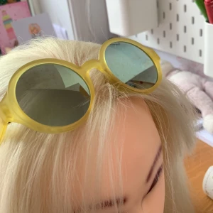 Runda gula solglasögon - Coola solglasögon med rund gul ram och mörka glas. Ramen är i plast och har en matt finish som ger en modern vibe. Perfekta för att sticka ut och ge din stil en färgklick. Passar dig som gillar retro och lekfulla accessoarer.