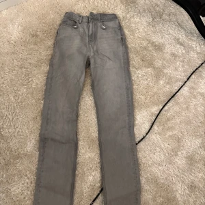 Grå raka jeans - Säljer ett par grå jeans med rak passform och klassisk femficksdesign. Byxorna har normal midja och är tillverkade i ett mjukt jeanstyg som passar perfekt till en avslappnad stil.