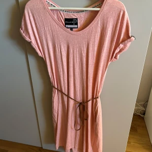 Ljusrosa klänning från Pelle P - Superfin ljusrosa klänning från Pelle P med rund halsringning, korta ärmar och ett smalt knytbälte i midjan. Klänningen är i mjuk bomull och har en avslappnad passform som är perfekt för varma dagar. Den är aldrig använd🩷