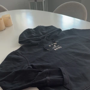 Svart t-shirt med Bruce Lee-tryck från BOSS - ✨ Säljer en exklusiv och eftertraktad svart hoodie med stort, ikoniskt tryck av Bruce Lee på baksidan, komplett med texten “BOSS” i elegant guld—en riktig eyecatcher! 🎯  🖤 Toppenskick – 10/10 🌟 Klassisk, rund halsringning och korta ärmar – stilren design som sitter snyggt året runt. 💪 Svår att få tag på – ett unikt plagg för dig som vill sticka ut. ✨ Perfekt för både vardagsstil och streetwear – skapar en cool look med minima