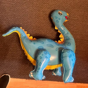 Folie Ballong Dinosaurie - Att kalasa med en dinosaurie är en häftig upplevelse - speciellt om dinosaurien i fråga är proppad med helium och svävar! Den här häftiga ballongen är en stämningshöjare av rang som garanterat kommer maxa roligheten på festen!  Folieballong Dinosaurie 🦕 är en dinosaurieformad ballong med taggig kropp. Kan fyllas med luft eller helium; med helium har den en flygtid på upp till 7 dagar. 