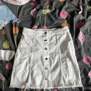 Vit jeanskjol från Perfect Jeans - Vit kort jeanskjol från Perfect Jeans med rå kant nertill och snygga sömdetaljer. Kjolen har knappar framtill hela vägen och en klassisk, rak passform. Perfekt för dig som gillar en clean och stilren look.