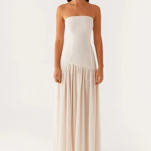 Ljus axelbandslös långklänning - Superfin axelbandslös långklänning i ljus beige ton. Klänningen har en figurnära överdel och ett flowy, rynkat kjolparti med hög slits på ena sidan. Perfekt för dig som gillar minimalistisk och elegant stil. Aldrig använd med prislapp!